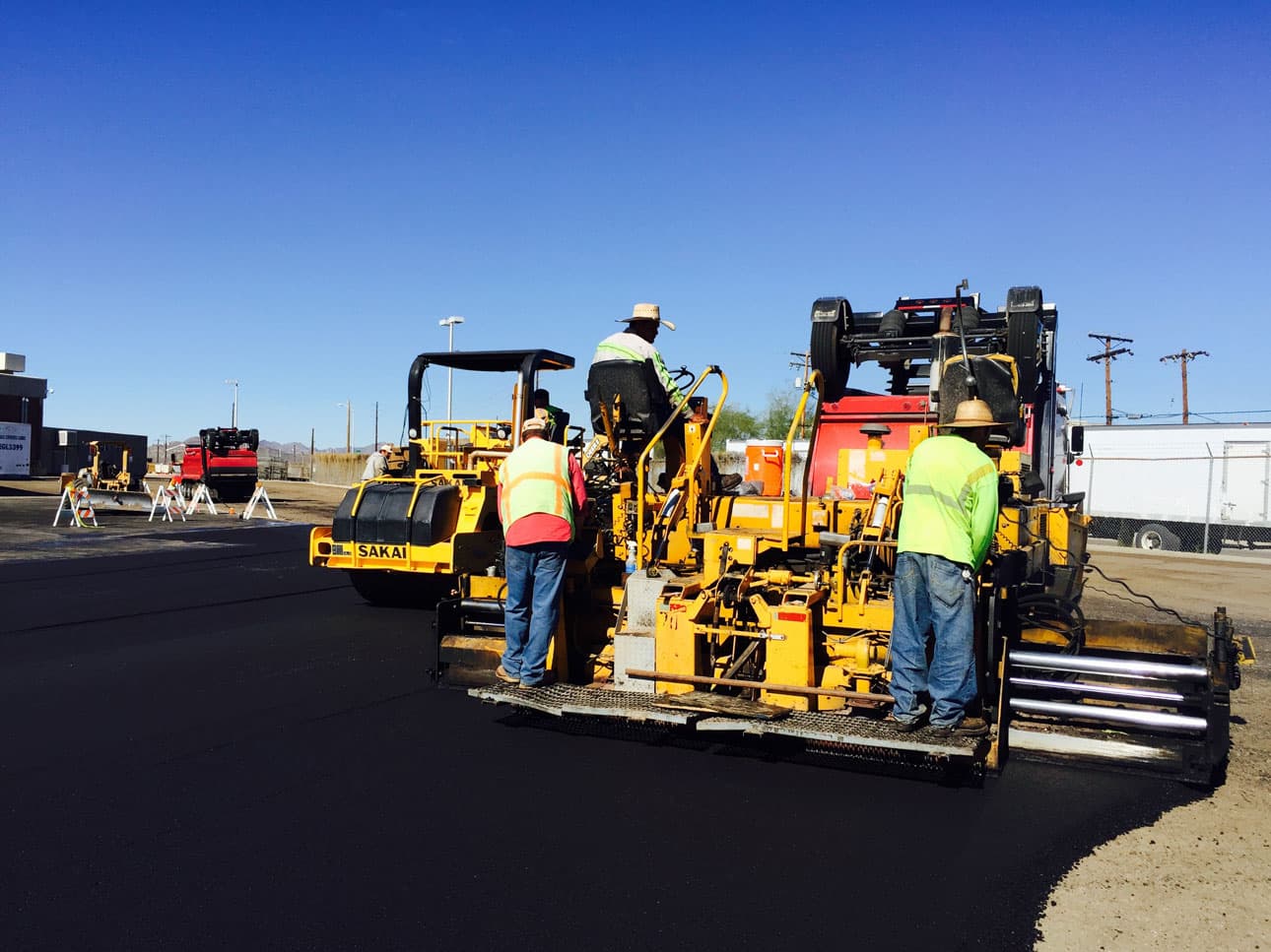 Paving crew operating a paver and roller on a fresh asphalt road